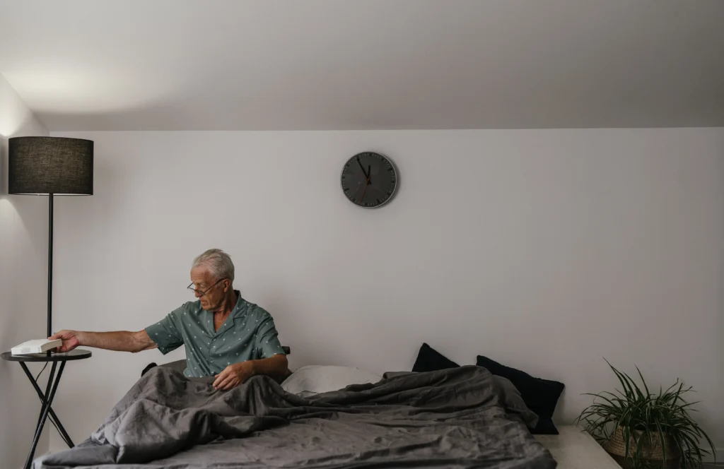 Elderly man sitting in bed putting something down on desk - winter safety tips for seniors